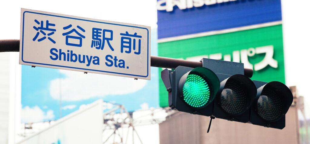 渋谷駅前の交差点に設置された青信号。光は緑がかった青色で点灯している。