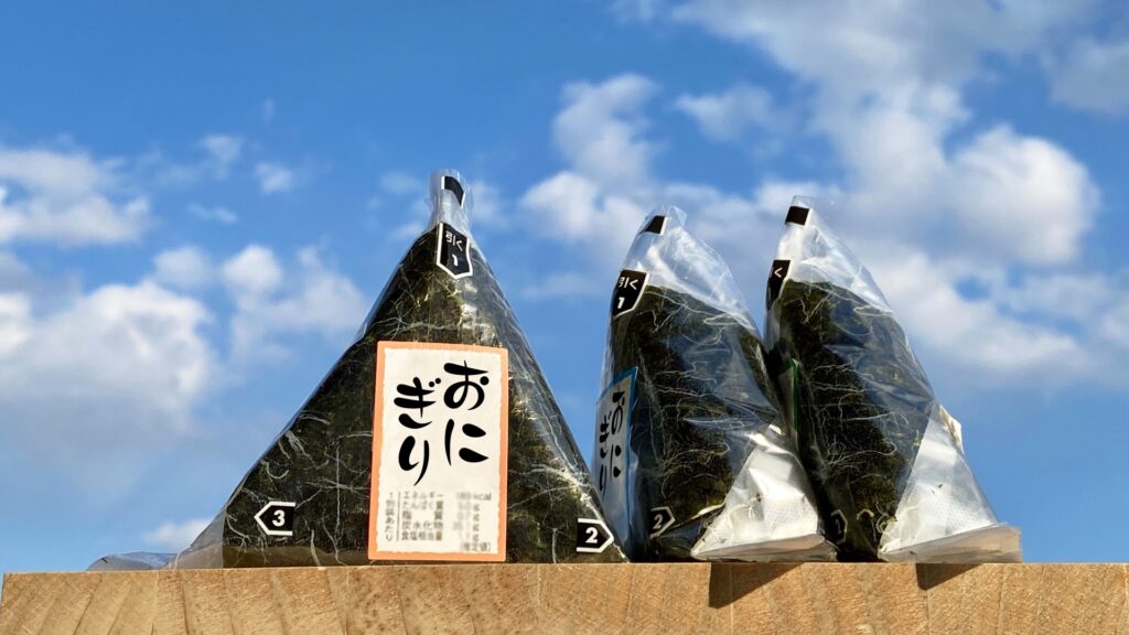 青空を背景に三角形のコンビニおにぎりが並んでいる様子