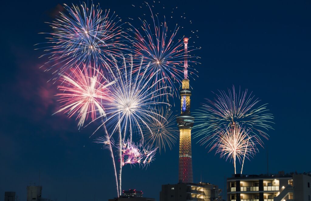 東京スカイツリーを背景に、多彩な大輪の花火が夜空を彩る現代の隅田川花火大会の様子